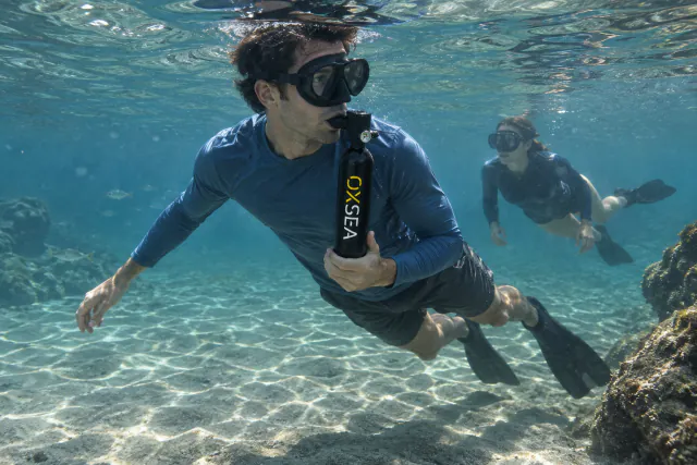 A diver explores a clear sandy bottom, breathing from an OX500.